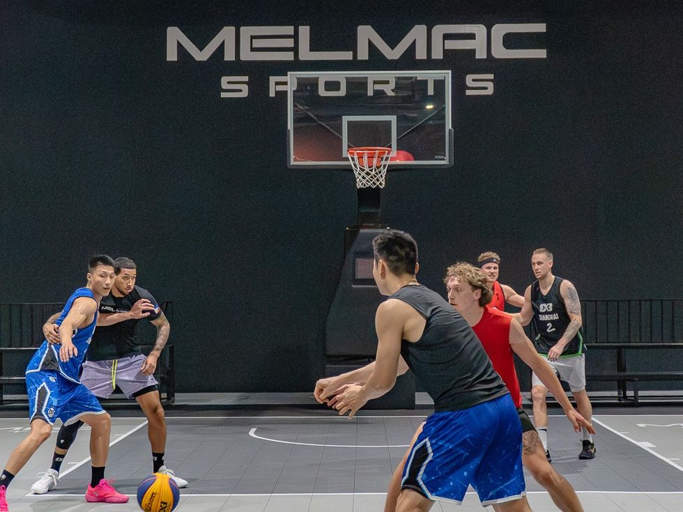 A 3×3 game in play beneath the Melmac Sports wall mark at Imus