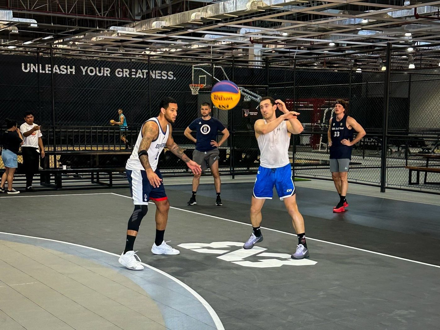 A 3x3 game in play beneath the Unleash Your Greatness wall at Imus