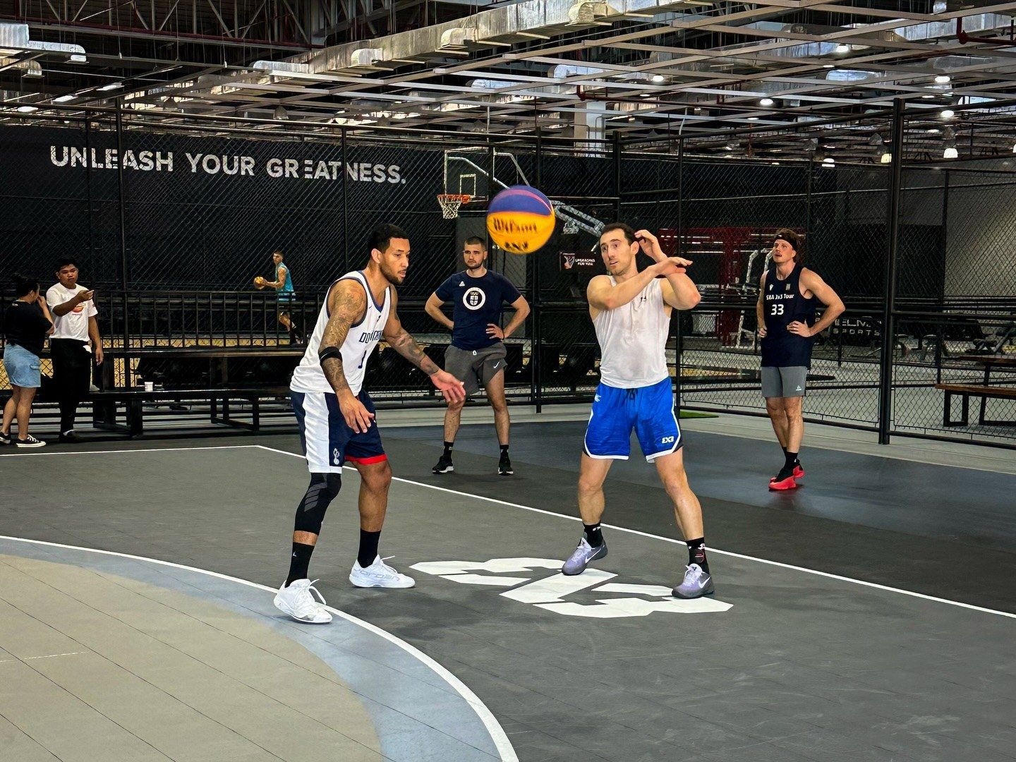 A 3x3 game in play beneath the Unleash Your Greatness wall at Imus