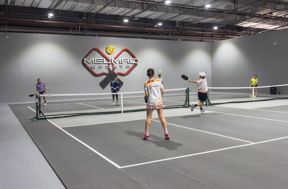 Players in a doubles rally across two pickleball courts at Melmac Sports Imus