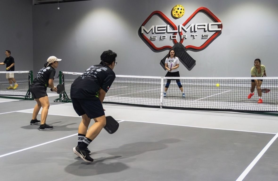 Four players mid-rally on an indoor pickleball court at Melmac Sports Imus