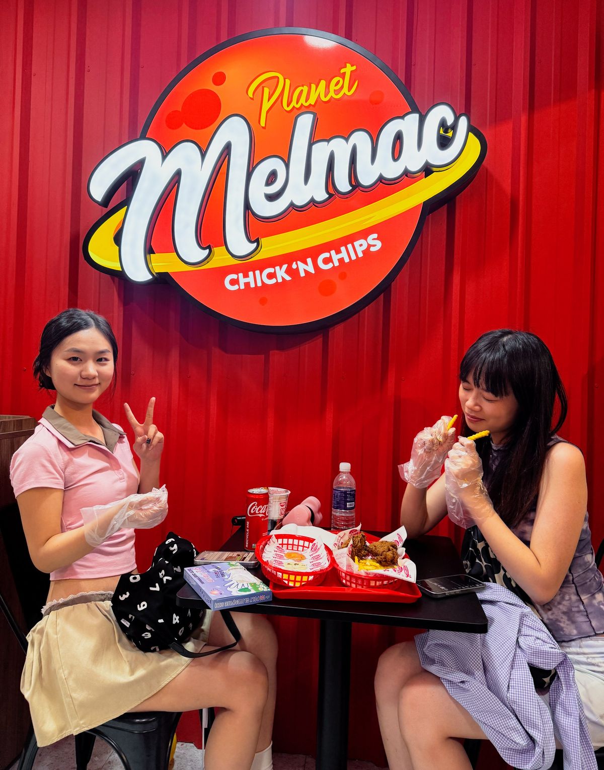 Two customers eating beneath the Planet Melmac sign in Singapore