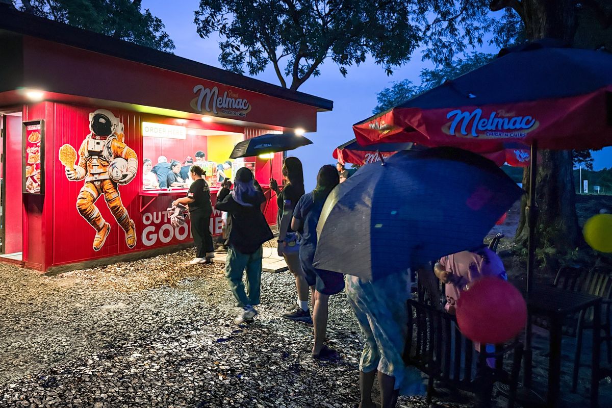 The lit Planet Melmac kiosk at Villar City at dusk, with customers queuing