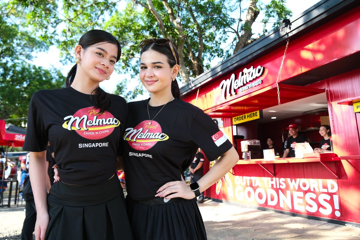 Two women in Planet Melmac shirts posing beside the kiosk at Villar City