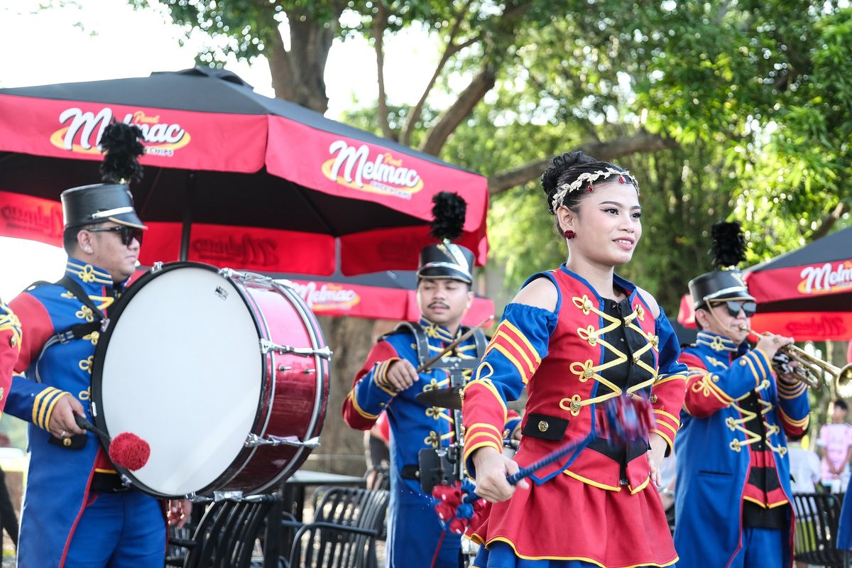A marching band with a bass drum performing under Planet Melmac umbrellas at Villar City