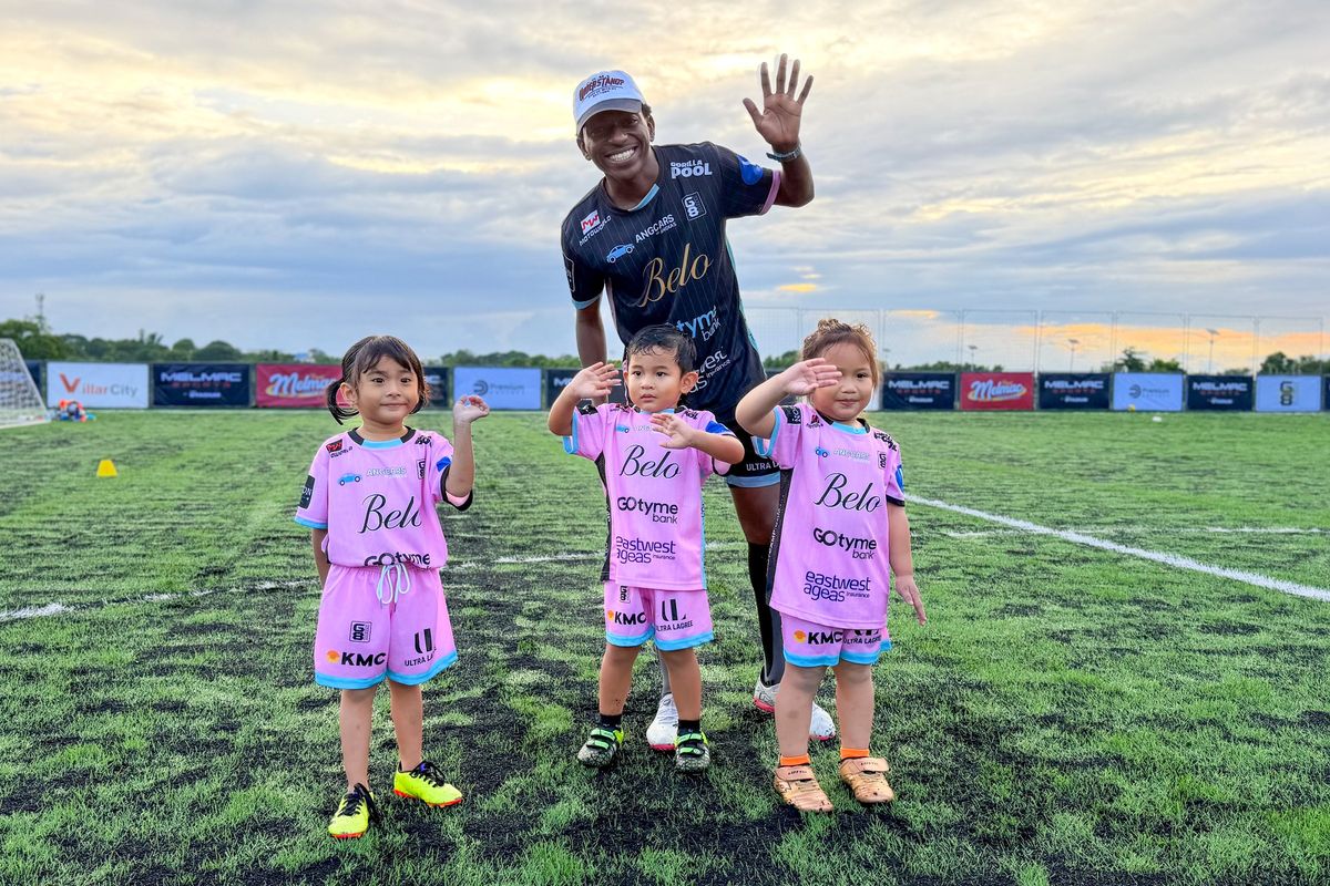 A coach waving beside three small players in Melmac kit at Villar City