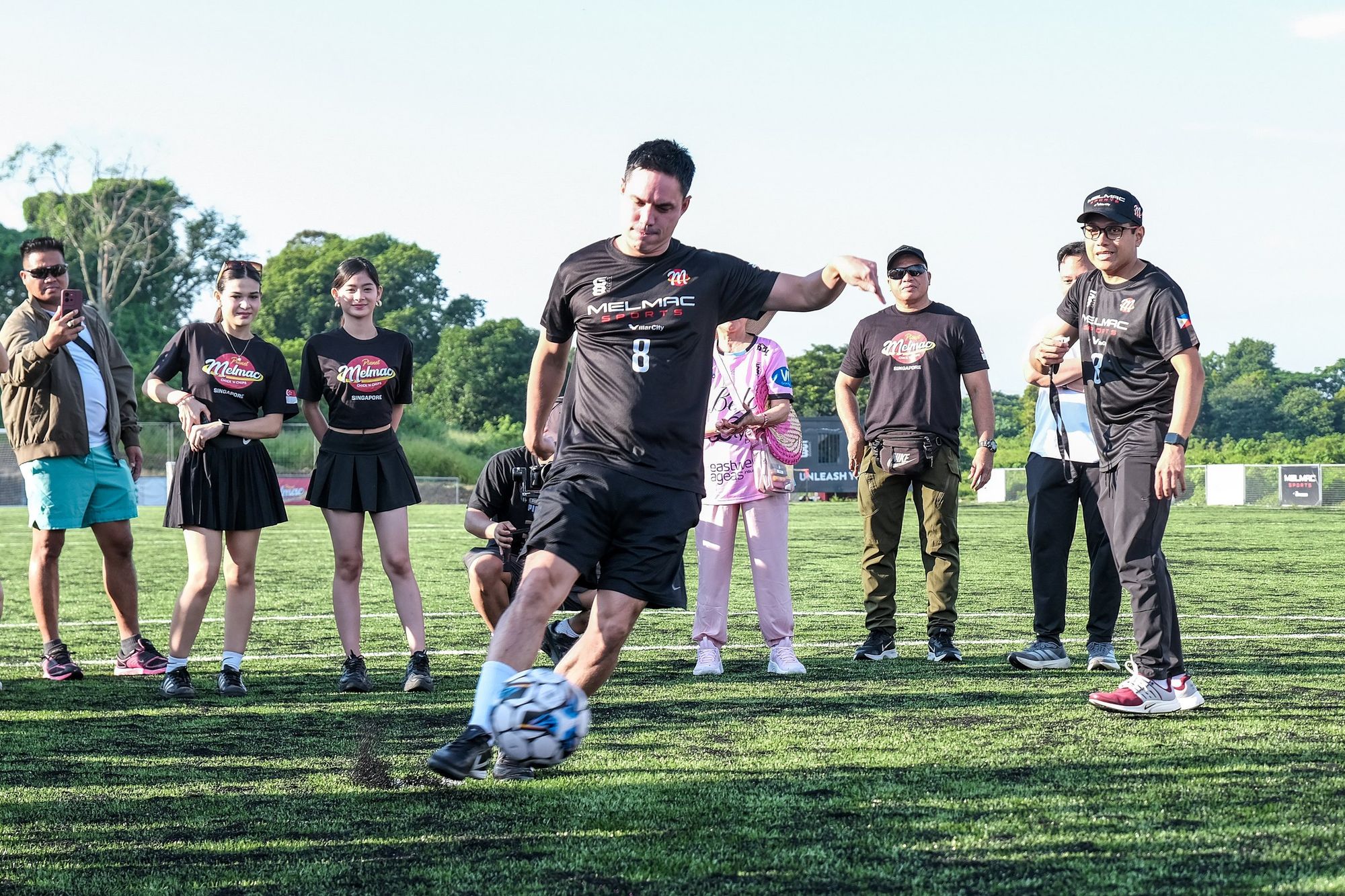 A player in a Melmac jersey kicking a ball as guests look on at Villar City