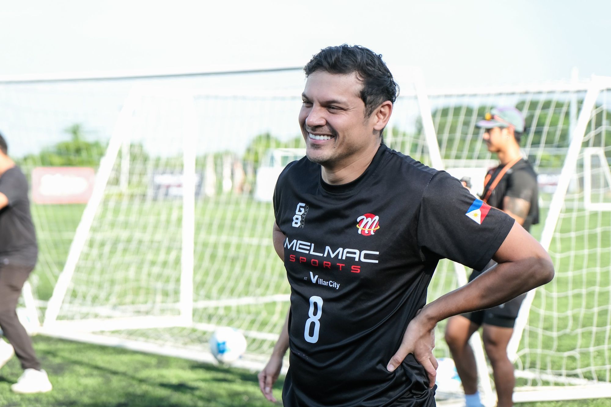A smiling player in a black Melmac number 8 jersey on the pitch at Villar City