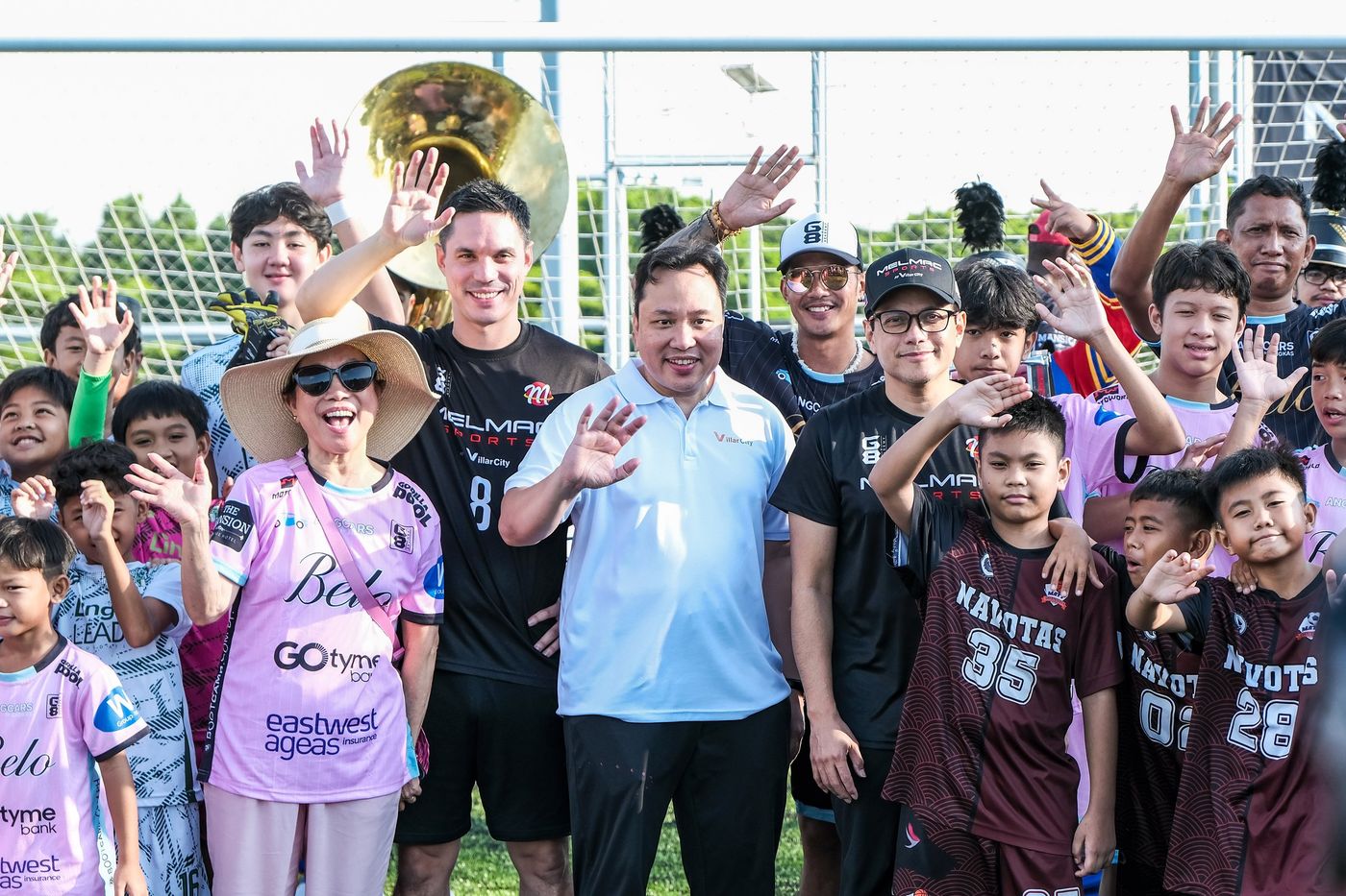 Children, players and guests waving at the camera on the pitch at Villar City