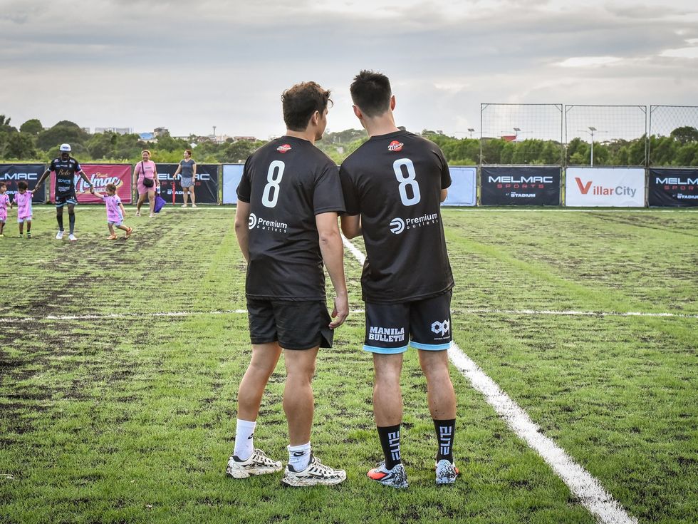 Two Melmac players standing on the pitch at Villar City as training runs behind them